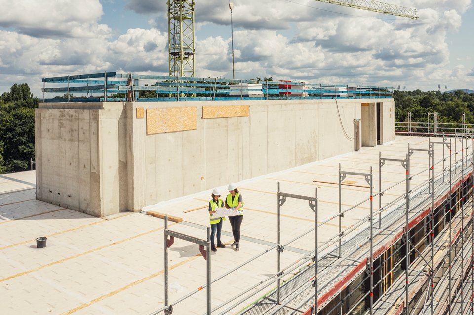 Zwei Personen stehen auf einem Dach in Sicherheitskleidung.