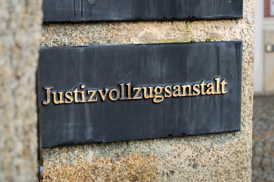 Ein Schild an der Wand eines Gebäudes. Es sagt "Justizvollzugsanstalt".